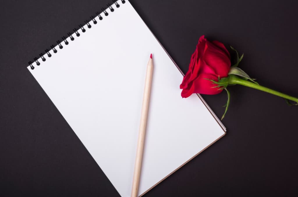 Open sketchbook with a pencil and a red rose on a dark background